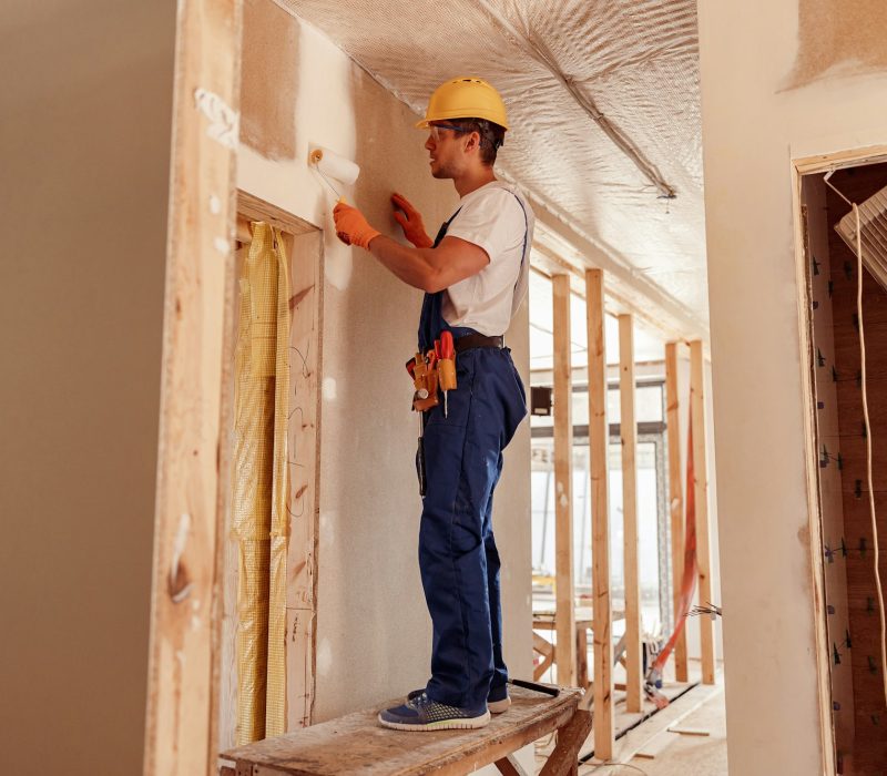 Male builder painting wall in house under construction